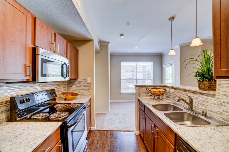 Kitchen with chestnut cabinetry, speckled granite countertops, tile backsplash, stainless steel appliances, and hard surface flooring - eaves North Dallas