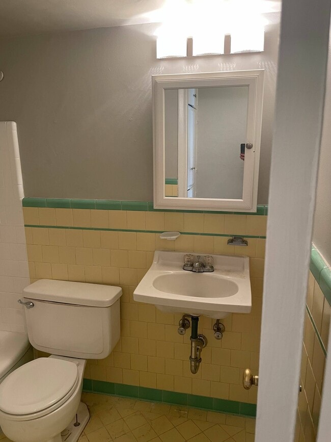 Charming vintage bathroom with pastel yellow and green tile decor, featuring a well-maintained sink and toilet, illuminated by soft lighting. - Lucca Apartments