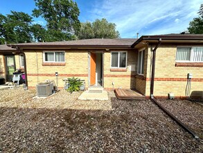Charming brick exterior of a cozy home with a welcoming open door, surrounded by a low-maintenance rock garden and lush greenery. - Flats at 16th