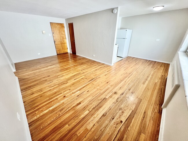 Experience the warmth of this inviting wood-floored living area, seamlessly leading into a functional kitchen. - The Birney Apartments