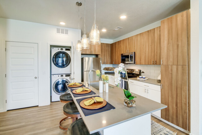 Kitchens feature oak upper and white lower cabinetry, grey quartz countertops, white subway tile backsplash, kitchen island or breakfast bar, and luxury vinyl plank flooring - Avalon Flatirons