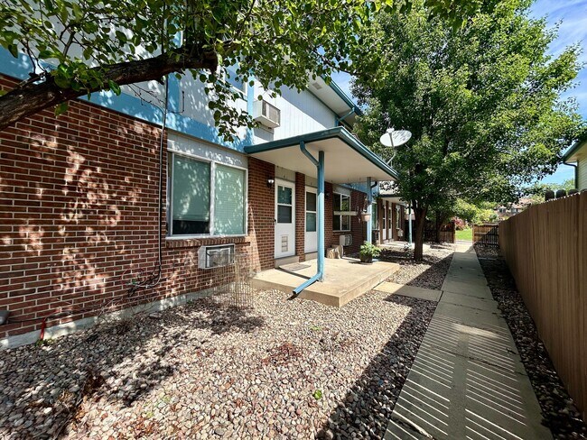 Charming brick apartment exterior with lush greenery and a cozy concrete patio. - 10756 West 12th Lane