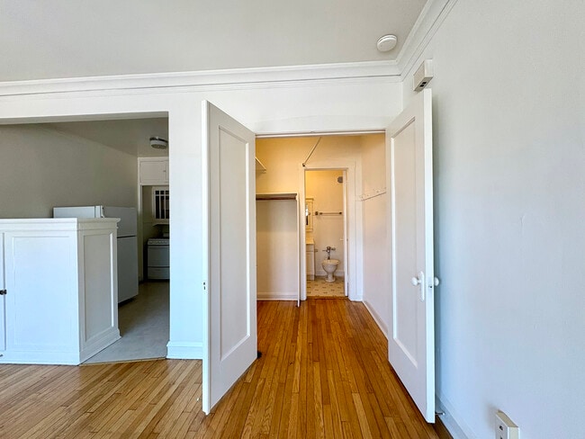 Inviting apartment interior showcasing a bright hallway with wooden flooring, leading to a kitchen and bathroom, featuring elegant white doors. - Ivanhoe