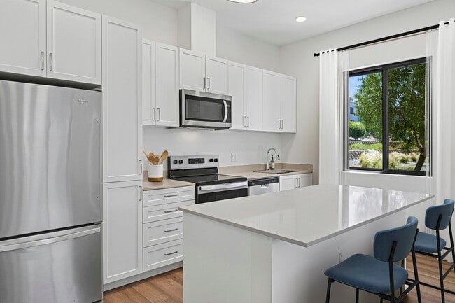 Freestanding Home kitchen with stainless steel appliances, white cabinetry, beige quartz countertops, and hard-surface flooring - eaves San Marcos