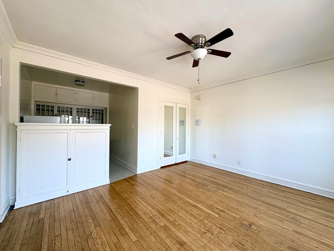 Bright and spacious living room with elegant hardwood floors, a classic ceiling fan, and built-in cabinets in an inviting open layout. - Ivanhoe