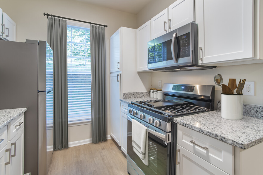 Renovated Package II kitchen with stainless steel appliances, white speckled quartz countertops, white cabinetry, and hard surface flooring - Avalon at Traville