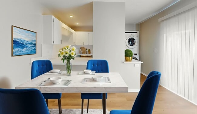 Bright dining area with elegant table set for four, featuring blue chairs and a modern kitchen in the background. Vibrant ocean artwork and fresh flowers add charm. - Villas of Stone Ridge