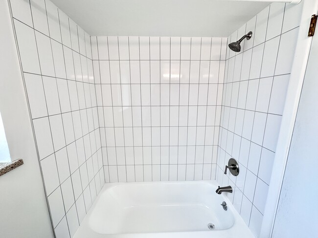Modern bathroom with sleek white tiles and a stainless steel shower fixture. - Columbine Plaza