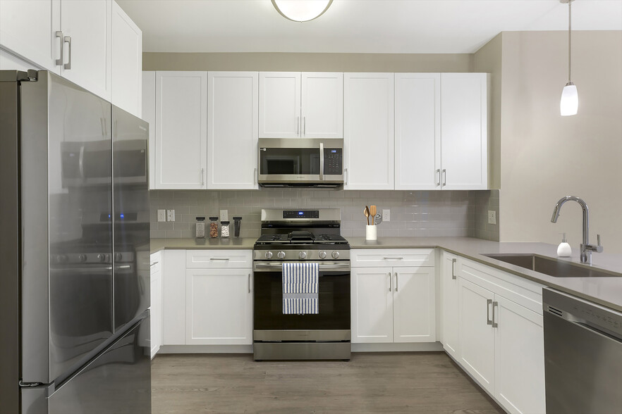 Renovated Package II kitchen with grey quartz countertops, white cabinetry, grey tile backsplash, stainless steel appliances, and hard surface flooring - Avalon Marlborough