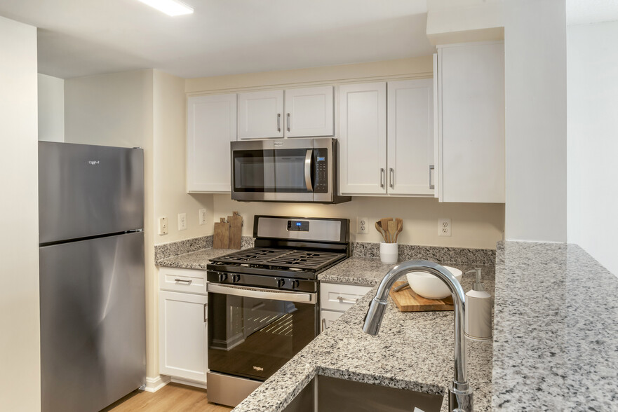 Renovated Package I kitchen with white cabinetry, granite countertops, stainless steel appliances, and hard surface flooring - Avalon Courthouse Place