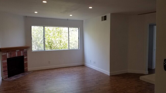 Living Room with wood panel floors, gas fireplace, LED lighting and red pipebrush tree in window. - 14126 Tiara St