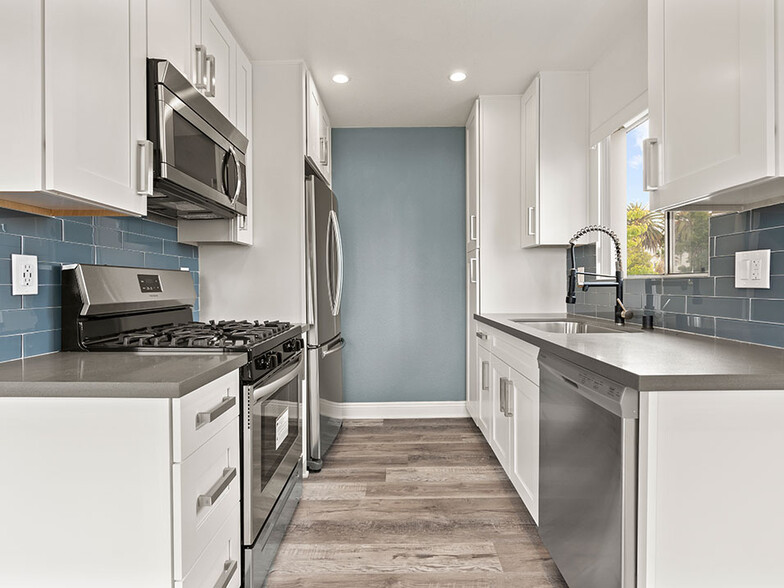 Blue tiled kitchen with stainless steel oven, microwave, and fridge. - Vinton Apartments