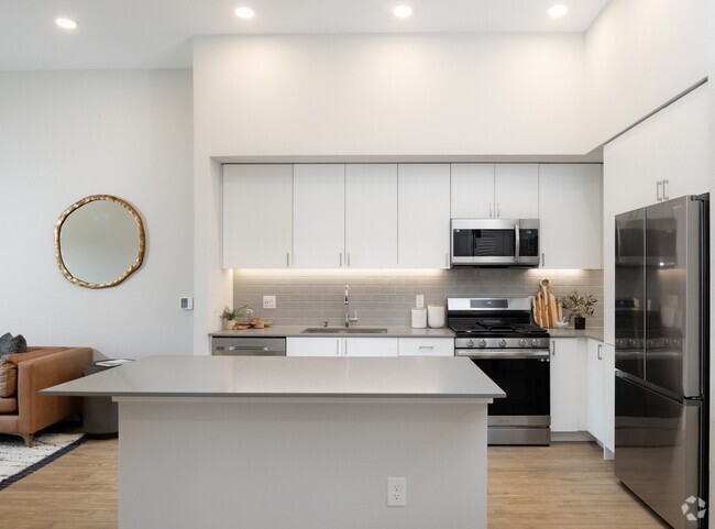 Kitchen with grey quartz countertops, white cabinetry, grey subway tile backsplash, stainless steel appliances, and hard surface flooring - Avalon Bothell Commons