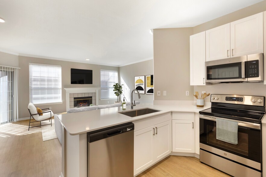 Renovated Package I kitchen with stainless steel appliances, white speckled quartz countertop, white cabinetry, and hard surface flooring - Avalon Addison