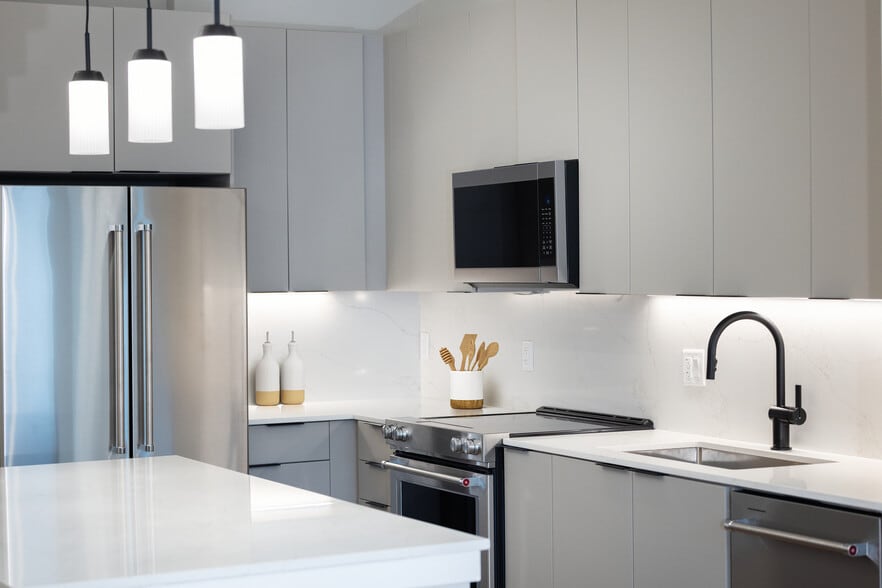 Signature Collection kitchen with stainless steel appliances, light grey cabinetry, marbled quartz countertops and backsplash, under-cabinet lighting, and pendant lighting - Avalon at Becker Farm