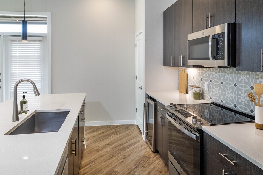 Kitchens with stainless steel appliances, wine fridges, quartz countertops, tile backsplash, and hard surface flooring - Avalon Townhomes at Bee Cave