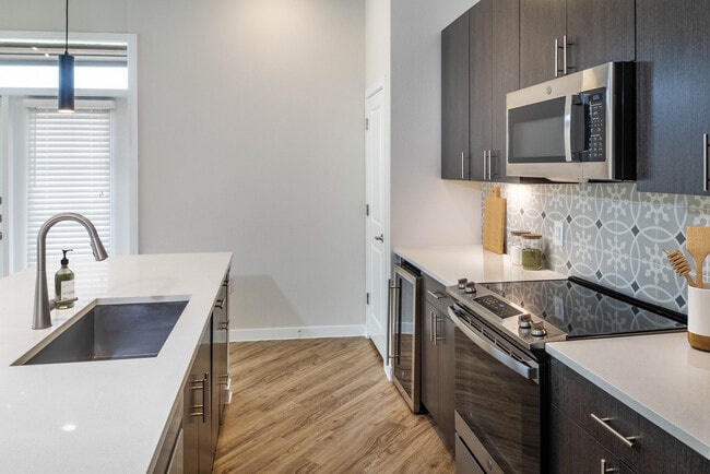 Kitchens with stainless steel appliances, wine fridges, quartz countertops, tile backsplash, and hard surface flooring - Avalon Townhome Collection Bee Cave