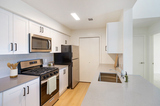 New Apartments kitchen with new stainless steel appliances, grey quartz countertops, grey subway tile backsplash, and hard surface flooring - Avalon Commons