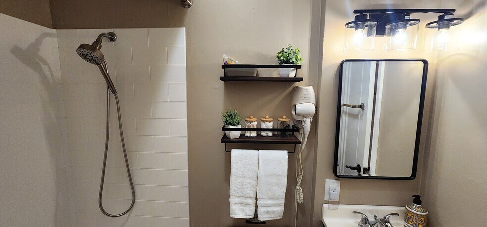 Updated shower with multi-function head and view toward vanity and stocked shelves. - 822 E 4th St