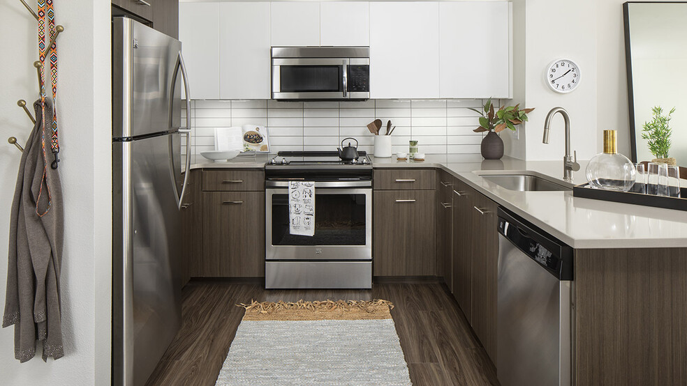 Apartment kitchen with stainless steel appliances, quartz countertops, and wood-style flooring. - Griffis Cherry Creek