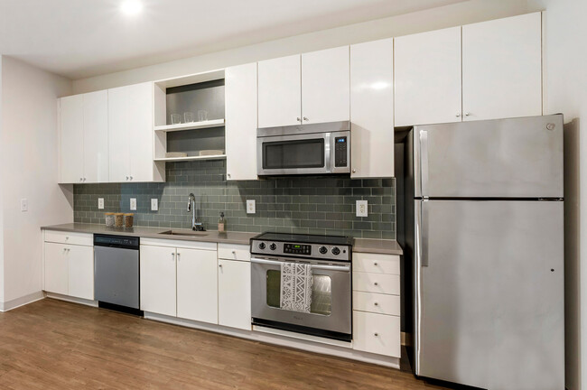 Renovated Package I kitchen with stainless steel appliances, grey quartz countertops, white cabinetry, grey tile backsplash, and hard surface flooring - AVA H Street