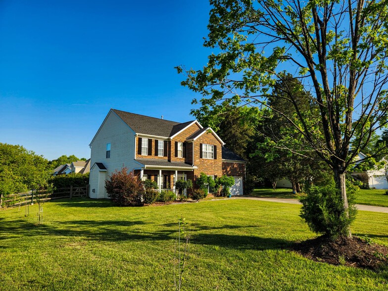 Side view with lush lawn, mature trees, and welcoming porch. - 7801 Peach Blossom Ct